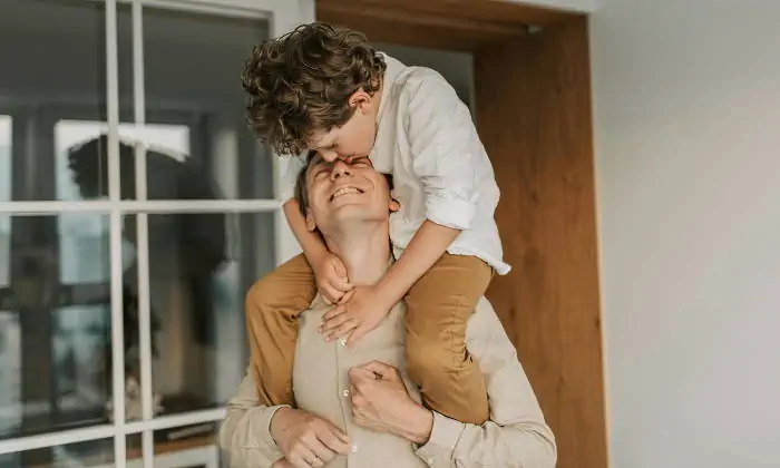 Padre cargando a su hijo en hombros mientras recibe un beso
